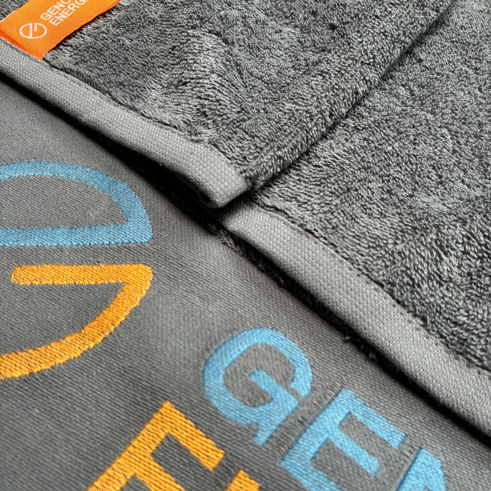 Handtuch Bordüreneinwebung in Grau: zweifarbiges Logo in Blau und Orange, Webetikett am Rand